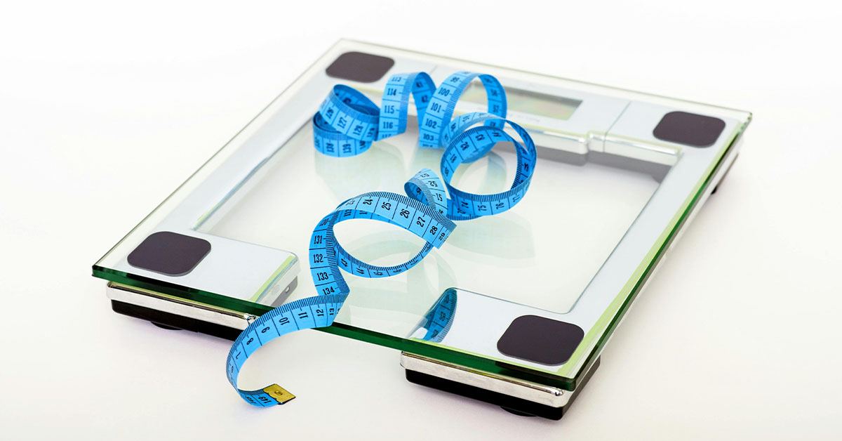 A glass bathroom scale with a blue measuring tape coiled on top, symbolizing medical weight loss and health monitoring.